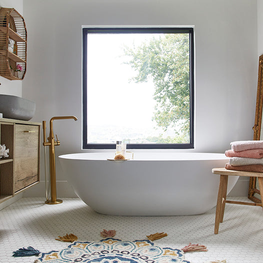 A biophilic interior space with light shining into the room. Bathroom image with focus placed on large window over bath tub, bringing nature inside.